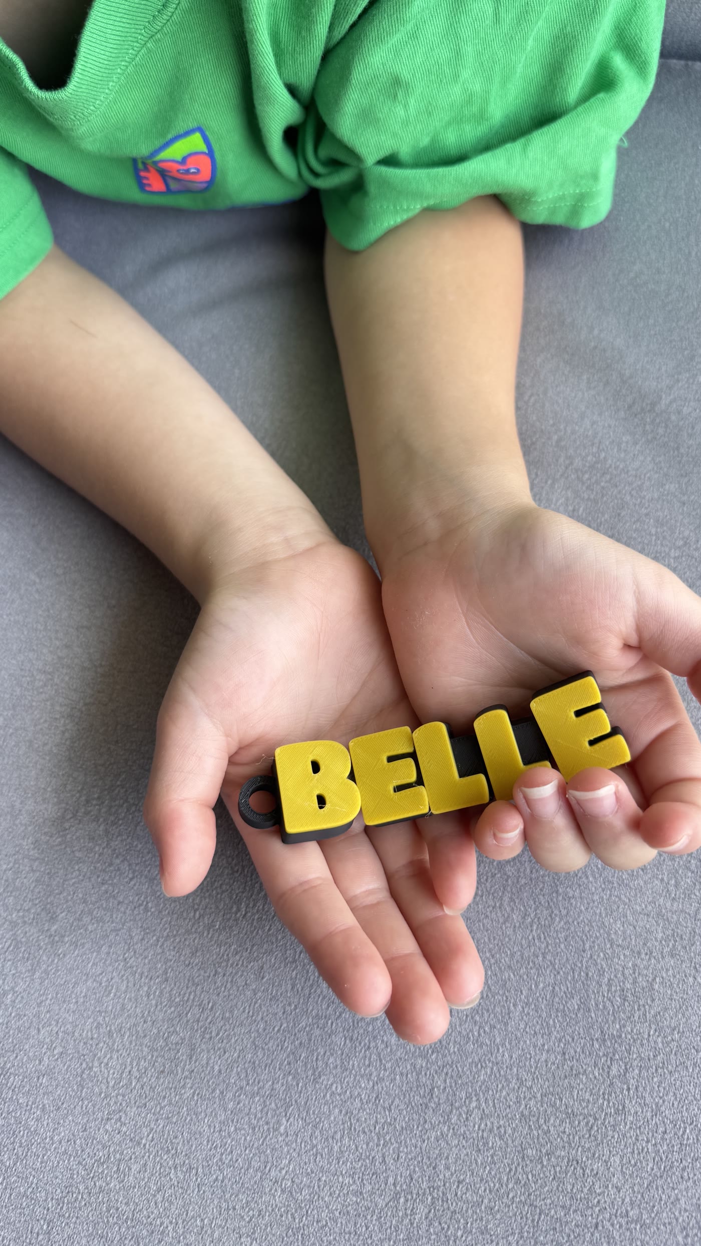 A finished name keychain shown in a child's hands for scale